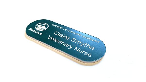 Teal Green with white text in the shape of a pill name badges, Logo to the left-hand side of the badge displaying Petcare. The top line says Avenue Veterinary Surgery underneath a new line saying Claire Smythe and the 3rd line says Veterinary Nurse. The badge is on a clean white background