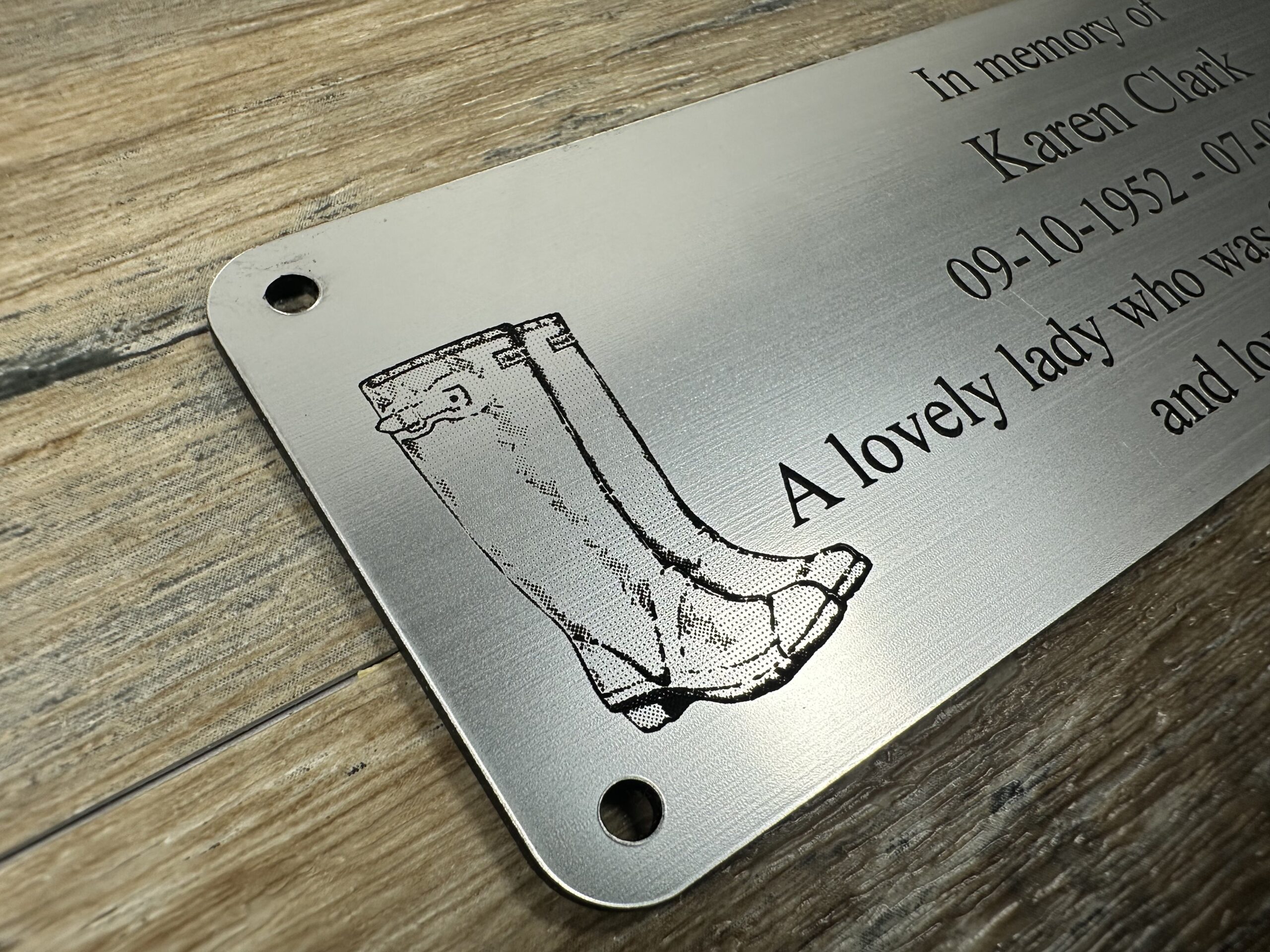 Acrylic Bench Plaque (Wellington Boot) Custom 6x2 inch brushed silver acrylic memorial plaque featuring a laser-engraved wellington boot and text engraved. The plaque has a metallic finish and pre-drilled holes, shown resting on a rustic wood surface.